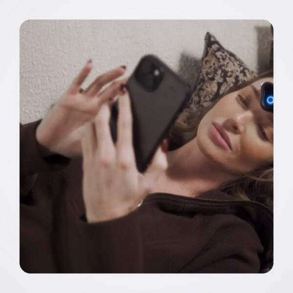 Woman resting with CEFALY Connected on her forehead while using the app on a smartphone