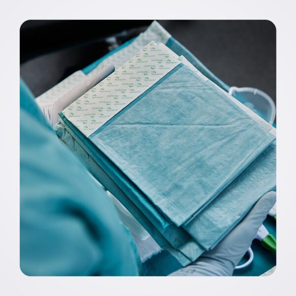 Gloved hands holding an opened ProcedurePak tray with folded drapes and components inside