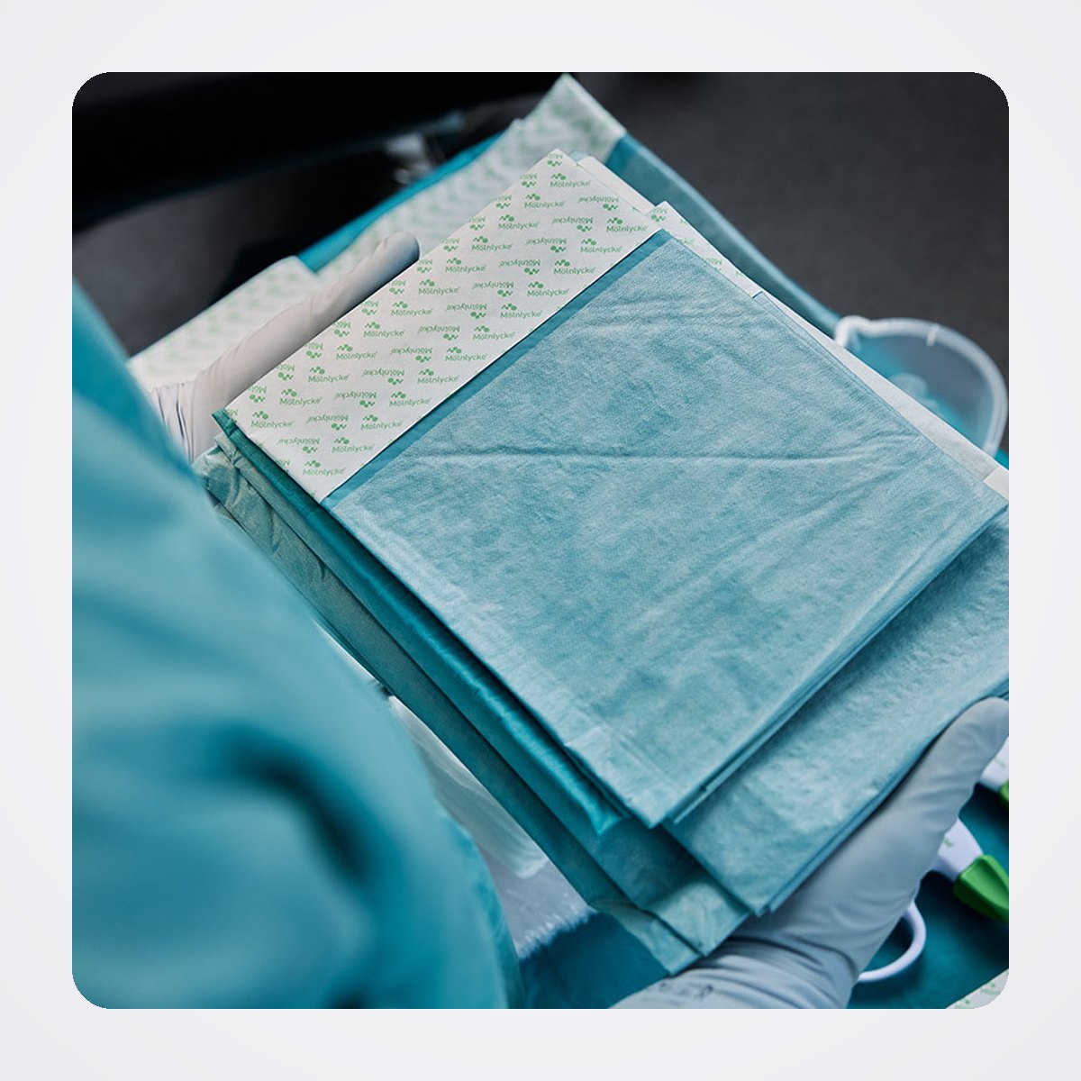 Mölnlycke ProcedurePak Custom Procedure Trays for the Operating Room 1 Gloved hands holding an opened ProcedurePak tray with folded drapes and components inside